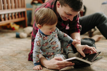 Glücklicher Vater zeigt seinem Sohn ein Bilderbuch, während er zu Hause auf dem Teppich sitzt - CAVF15562