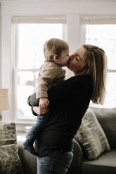 Mutter küsst ihren Sohn, während sie ihn im heimischen Wohnzimmer trägt - CAVF15573