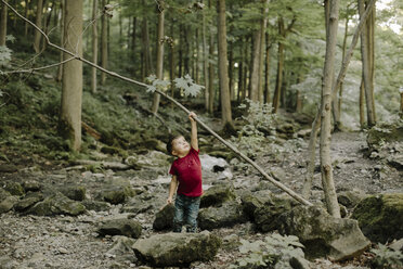 Verspielter Junge, der im Wald stehend einen Stock hebt - CAVF15582