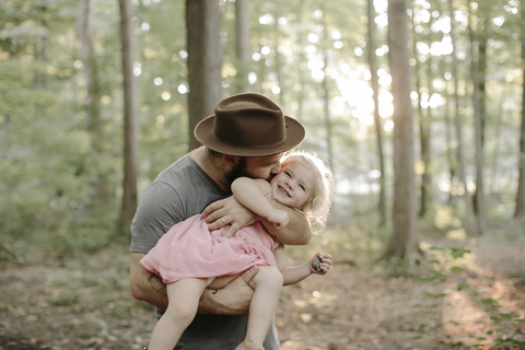 Vater mit Hut küsst Tochter im Wald stehend, lizenzfreies Stockfoto