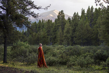 Frau im Wald stehend, während sie in eine Decke eingewickelt an Bäumen lehnt - CAVF15589