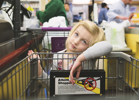 Gelangweiltes Mädchen mit Einkaufswagen im Supermarkt, lizenzfreies Stockfoto