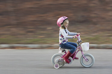 Happy girl riding bicycle on road by field - CAVF15601