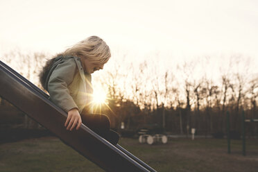 Seitenansicht eines fröhlichen Mädchens, das auf einem Spielplatz bei Sonnenuntergang auf einer Rutsche spielt - CAVF15606