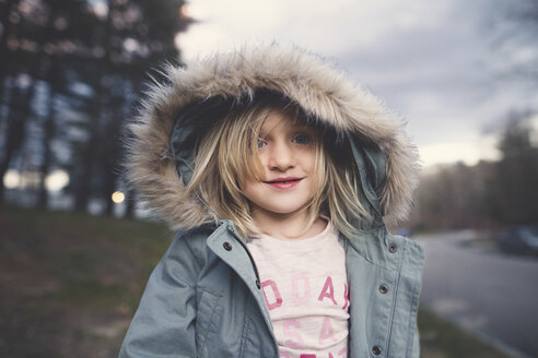 Cute smiling girl wearing fur hood standing on field - CAVF15608