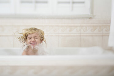 Mädchen mit geschlossenen Augen spritzt Wasser beim Baden in der Badewanne zu Hause - CAVF15609
