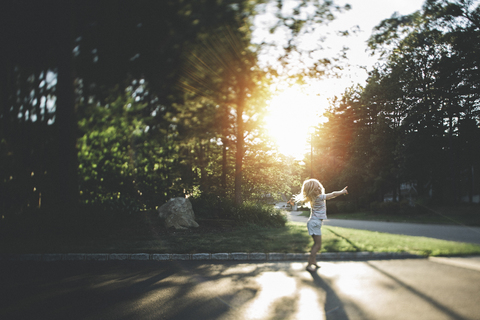 Cheerful girl dancing on road against trees during sunny day stock photo