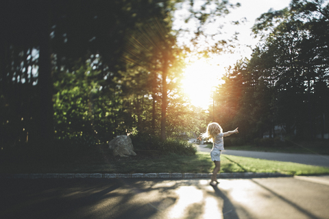 Fröhliches Mädchen tanzt auf der Straße gegen die Bäume an einem sonnigen Tag, lizenzfreies Stockfoto