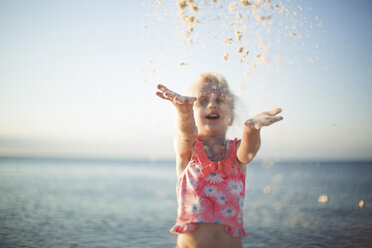 Cheerful girl playing with sand against sea at beach - CAVF15619