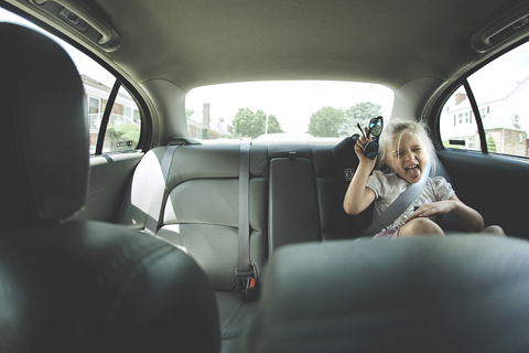 Playful girl with sunglasses sitting in car on sunny day stock photo