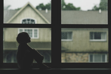 Thoughtful girl sitting on window sill against house - CAVF15627