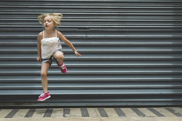 Girl jumping on sidewalk against shutter - CAVF15631