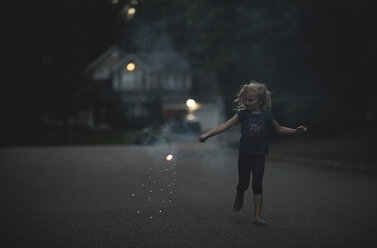 Girl playing with sparkler on road at dusk - CAVF15643