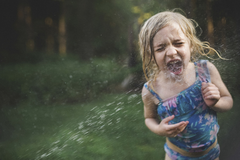 Mädchen genießt in der Wasserspritze im Hinterhof, lizenzfreies Stockfoto