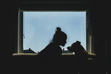 Mädchen und Hund auf dem Fensterbrett sitzend gegen den klaren Himmel - CAVF15646