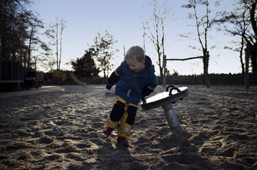 Full length of happy boy playing on sand in playground - CAVF15667