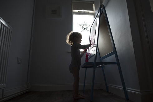 Silhouette eines Mädchens, das auf Papier malt, das an einem Whiteboard befestigt ist - CAVF15687