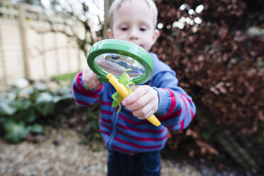 Playful boy looking artificial grasshopper through magnifying glass - CAVF15698