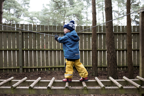 Full length of playful boy walking on jungle gym at playground stock photo
