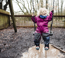 Mädchen in voller Länge auf einer Schaukel im Park während der Regenzeit sitzend - CAVF15725