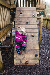 Rear view of girl rock climbing at park during rainy season - CAVF15726