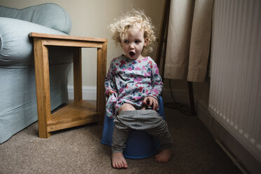 Girl with mouth open sitting on potty in room at home - CAVF15734