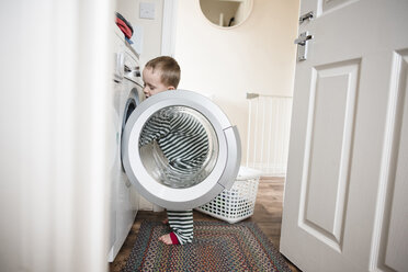 Junge, der zu Hause an der Waschmaschine steht, gesehen durch die Türöffnung - CAVF15737