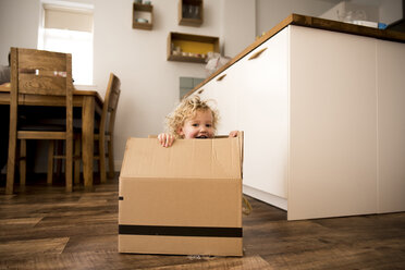 Portrait of happy girl sitting in cardboard box at home - CAVF15745
