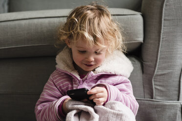 Girl using mobile phone while sitting by armchair at home - CAVF15752