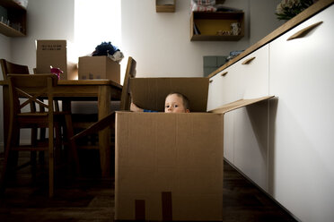 Portrait of playful boy sitting in cardboard box at home - CAVF15753