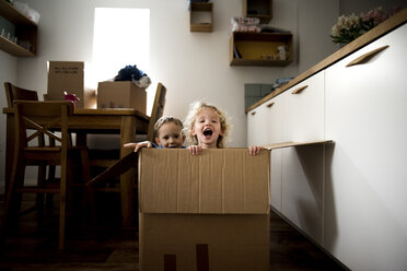 Portrait of cheerful siblings sitting in cardboard box at home - CAVF15754