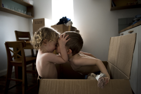 Bruder küsst Schwester, während er zu Hause im Karton sitzt, lizenzfreies Stockfoto