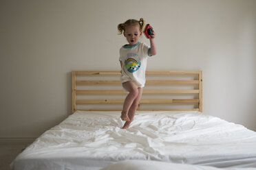 Verspieltes Mädchen springt in voller Länge auf dem Bett im Schlafzimmer - CAVF15766