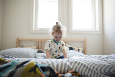 Cute girl looking down while sitting on bed against window - CAVF15778