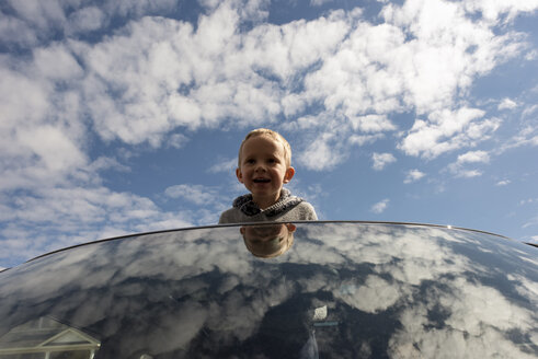 Fröhlicher Junge, der über das Sonnendach eines Autos gegen den bewölkten Himmel blickt - CAVF15781