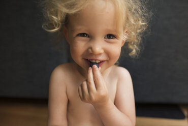 Porträt eines lächelnden Mädchens, das zu Hause sitzend Blaubeeren isst - CAVF15799