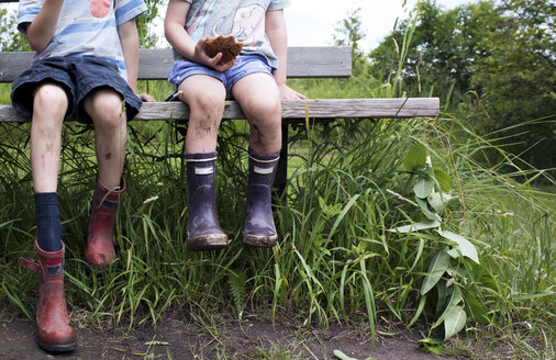 Niedriger Ausschnitt von Geschwistern mit schmutzigen Stiefeln, die auf einer Bank auf einem Feld sitzen - CAVF15804