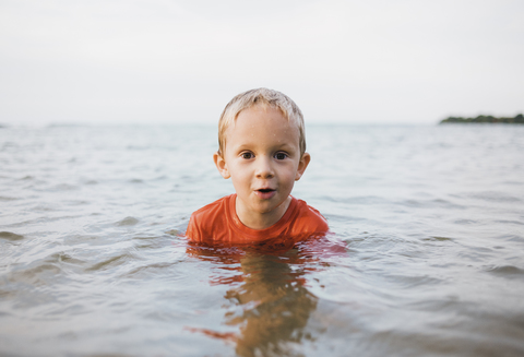 Porträt eines niedlichen Jungen im Meer gegen den klaren Himmel, lizenzfreies Stockfoto