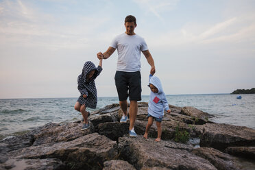 Vater und Kinder gehen auf Felsen am Meer gegen den Himmel - CAVF15825