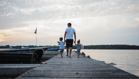 Rückansicht von Vater und Kindern, die auf dem Pier gegen den bewölkten Himmel laufen - CAVF15827