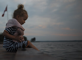 Mädchen sitzt auf dem Pier über dem Meer gegen den Himmel in der Abenddämmerung - CAVF15832