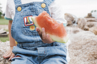 Mittelteil eines Mädchens, das eine angebissene Wassermelone hält, während es auf einem Bauernhof sitzt - CAVF15841