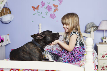 Lächelndes Mädchen spielt mit Hund auf Bett zu Hause - CAVF15871