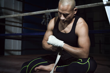 Älterer Mann wickelt einen Verband um seine Hand, während er im Fitnessstudio am Boxring sitzt - CAVF15875