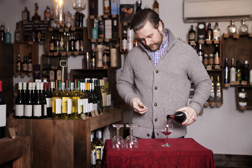 Männlicher Sommelier schenkt im Geschäft Rotwein in ein Glas ein - CAVF15909