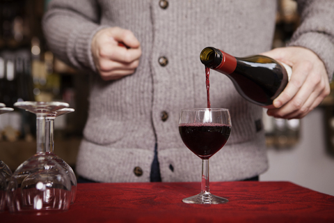 Mittelteil eines männlichen Sommeliers, der in einem Geschäft Rotwein in ein Glas gießt, lizenzfreies Stockfoto