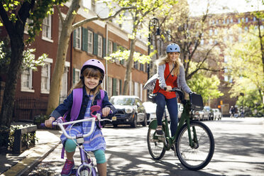 Portrait of happy mother and daughter riding bicycles on street - CAVF15941