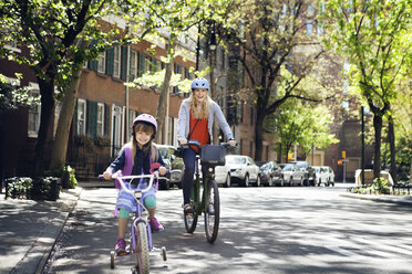 Porträt einer fröhlichen Mutter und ihrer Tochter, die auf der Straße Fahrrad fahren - CAVF15944