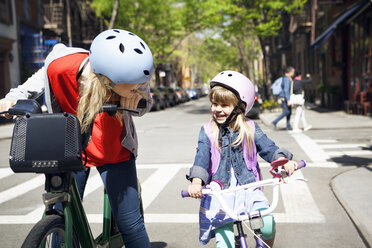 Happy woman talking to daughter while riding bicycles on street - CAVF15945