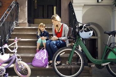 Mutter und Tochter unterhalten sich, während sie auf einer Treppe sitzen und im Vordergrund Fahrräder abgestellt sind - CAVF15948